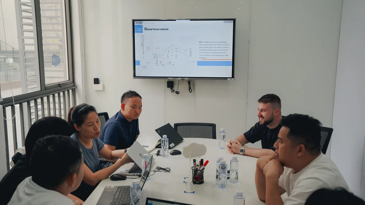 Peregrine Ship team in the Shenzhen office around a conference table, reviewing a Global Parcel Network slide on screen